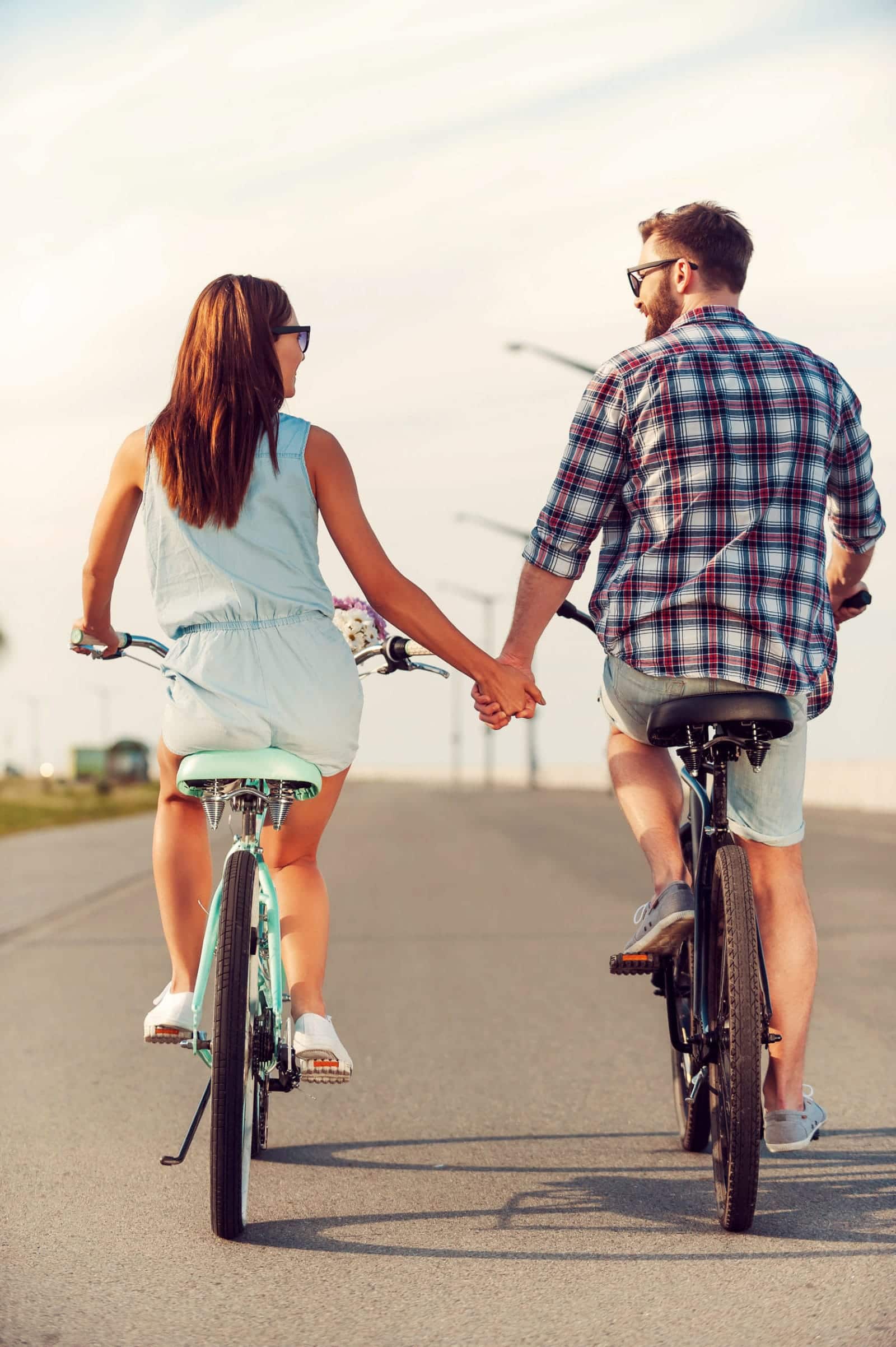 rear view of young couple holding hands while riding on bicycles along the road